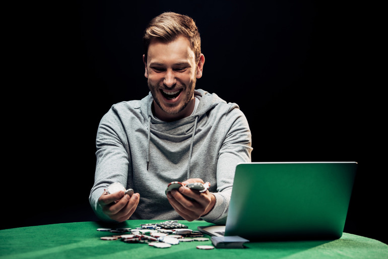 A man holding casino coins while playing online blackjack on a laptop.
