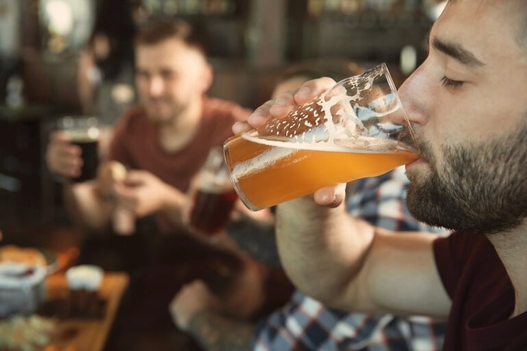 Man drinking craft beer at a bar with friends, reflecting modern entertainment habits.