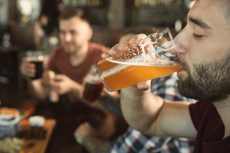Man drinking craft beer at a bar with friends, reflecting modern entertainment habits.