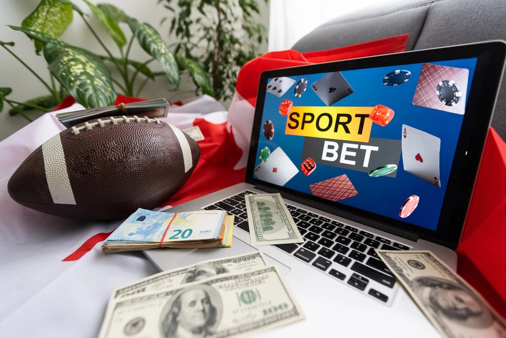 Laptop with sports betting graphics on it, with a football and cash on the table
