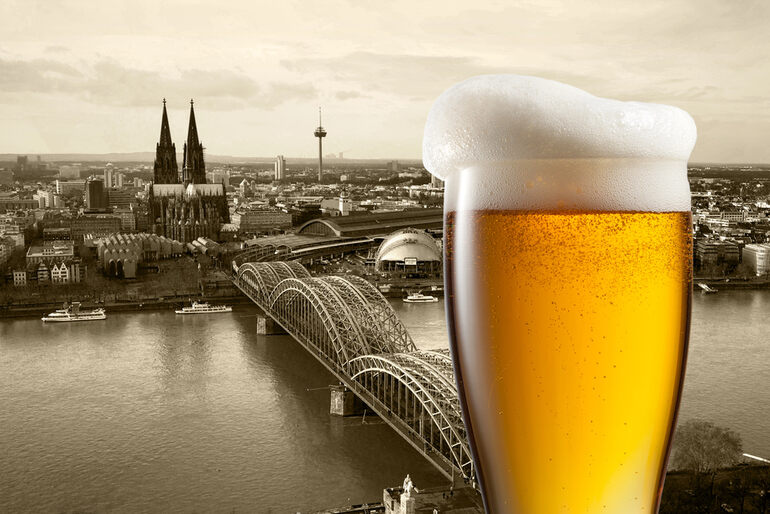 A glass of beer in front of an image of the city of Koeln.