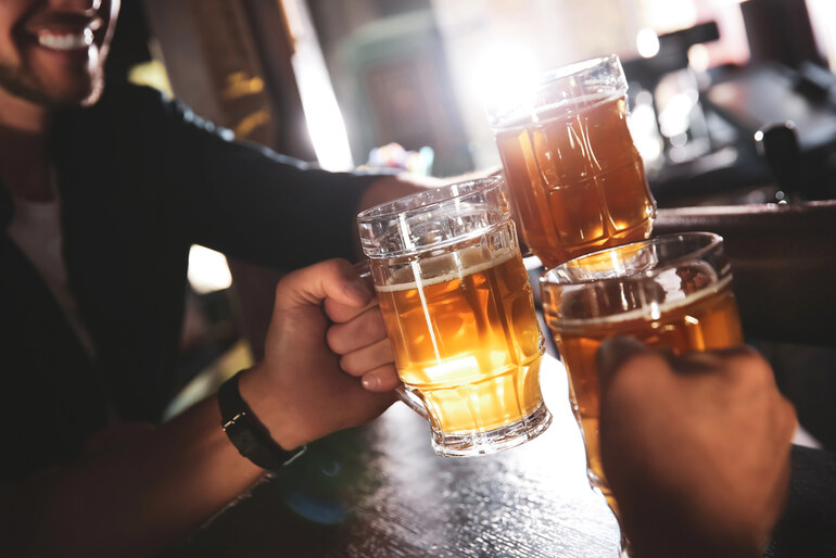 Friends clinking large mugs of craft beer in a bar, illustrating the topic of craft beer scams and misleading brewery practices