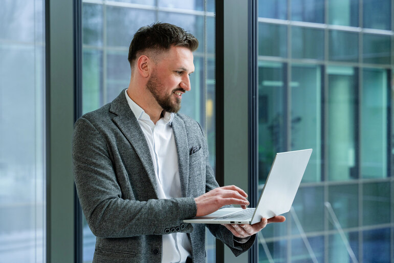 Man wearing a tailored blazer, dress shirt, and formal trousers while working on a laptop, illustrating key components of men’s formal attire