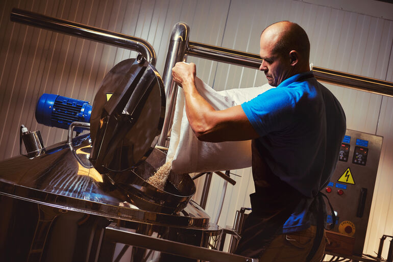 Brewer adding malt into a stainless steel brewing tank in a modern craft brewery