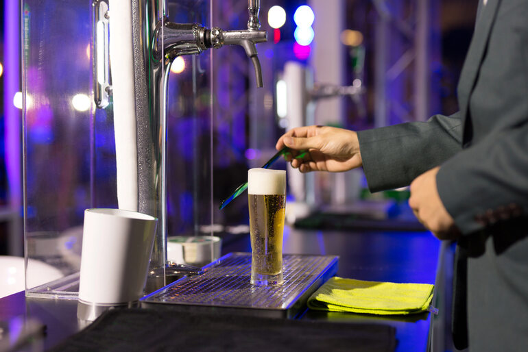 Person pouring a draft beer from a tap into a tall glass, with colorful bar lights in the background