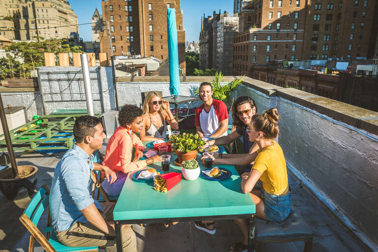 Friends enjoying drinks and food at a sunny rooftop bar with a city skyline view