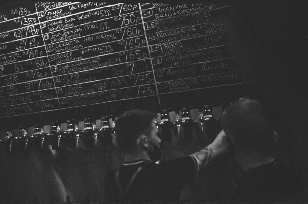 Black and white photo of a chalkboard menu above tap lines with many beer names.