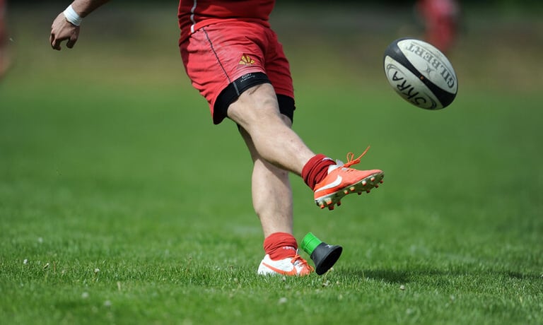 Rugby player kicking a ball on a grassy field during an outdoor match, capturing action and energy for a perfect day at the game
