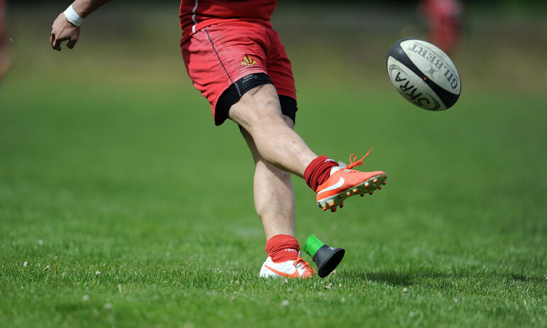 Rugby player kicking a ball on a grassy field during an outdoor match, capturing action and energy for a perfect day at the game