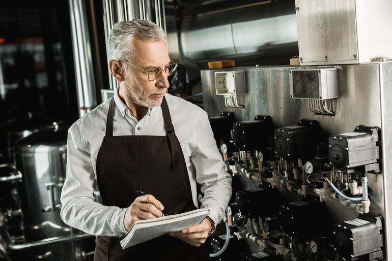 Worker monitoring industrial brewing process with notes