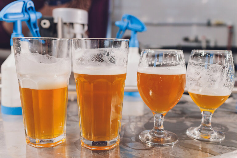 Various glasses of beer arranged on a wooden shelf