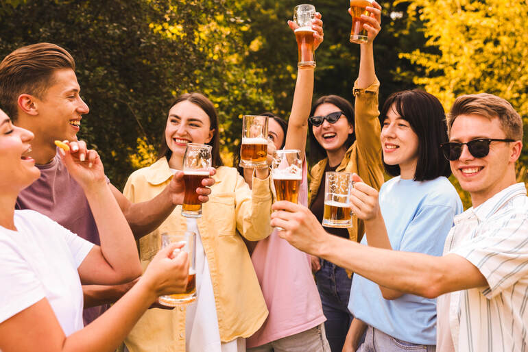 A group of young adults outdoors raising glasses of craft beer in a cheerful toast, reflecting the growing social appeal of beer tourism from Yakima to Bellingham
