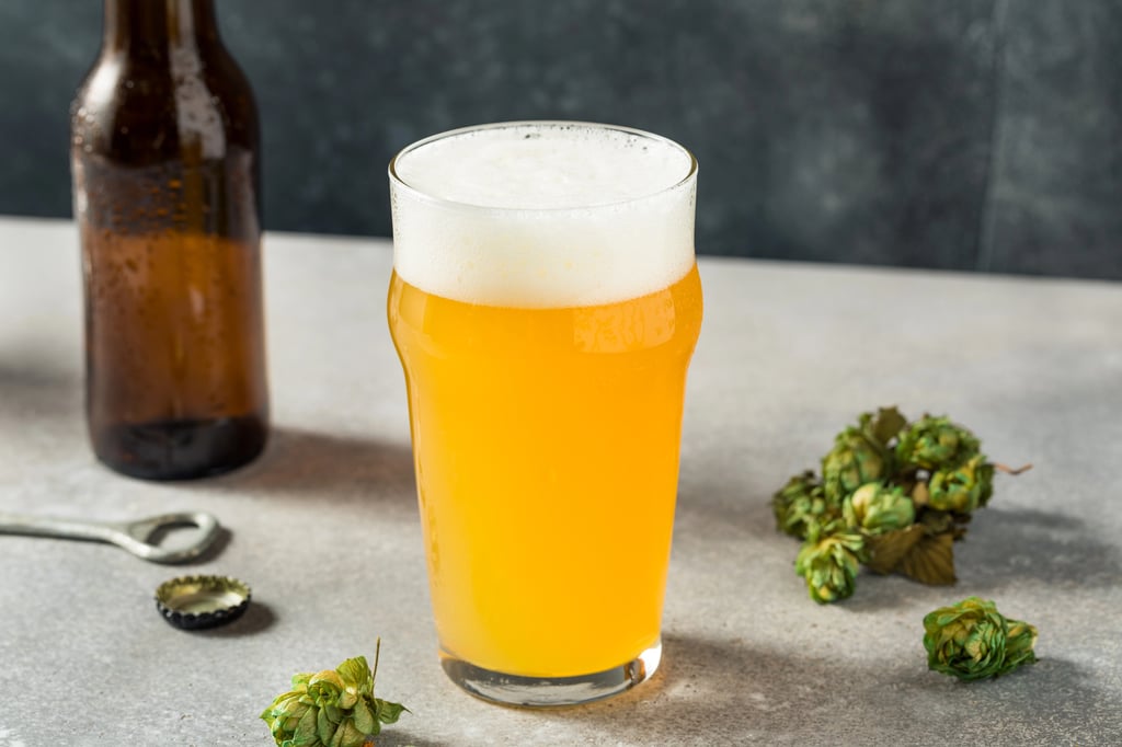 Hazy IPA glass and bottle on table with hops nearby.