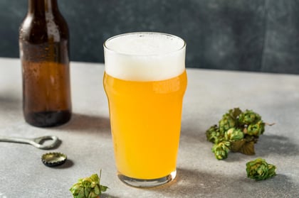 Hazy IPA glass and bottle on table with hops nearby.