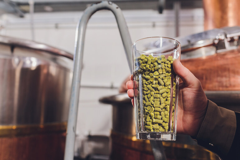 Man holding a glass jar filled with homemade beer during a DIY homebrewing process. 