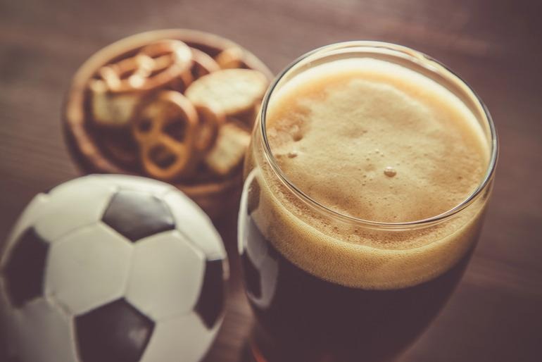A pint of dark session ale next to a mini soccer ball and a bowl of pretzels, representing balanced lifestyle and leisure choices.