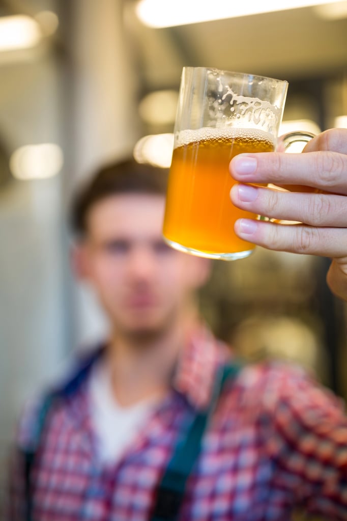 Man holding beer in front of his face to study its color and cloudiness.