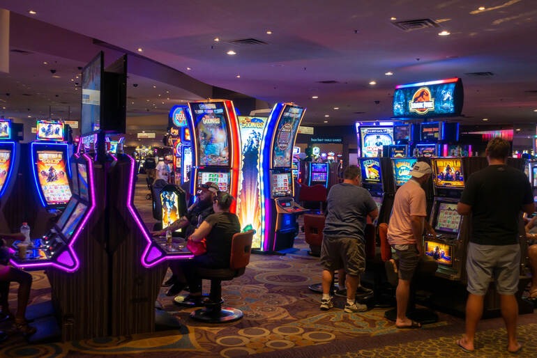 People playing brightly lit slot machines in a casino.