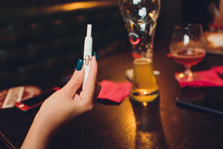 A girl holding a vape device at a table with drinks.