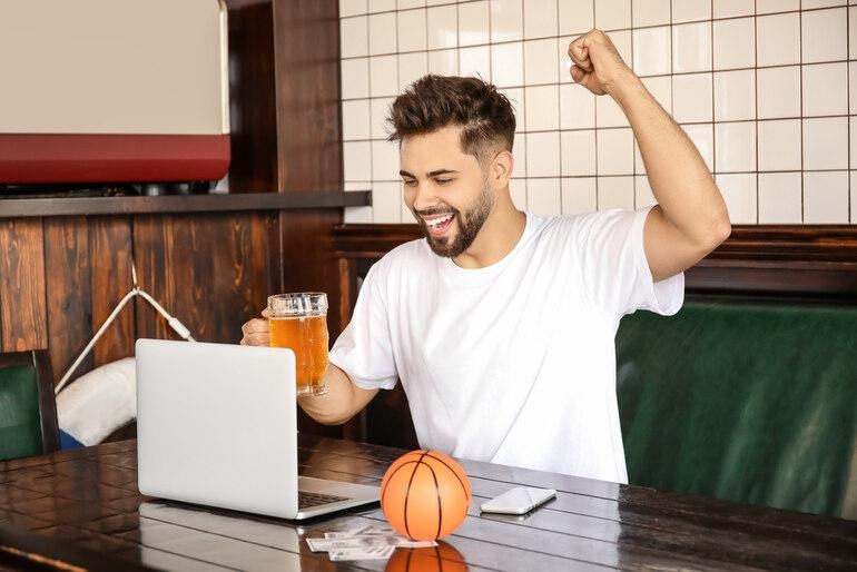 Man celebrating an NBA game on a laptop while holding a pint of beer.