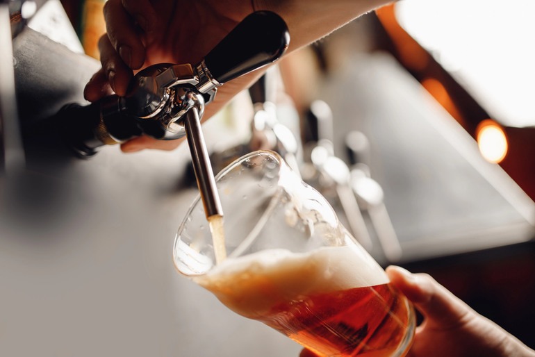 Bartender pouring craft beer from a keg into a glass at a taproom bar.