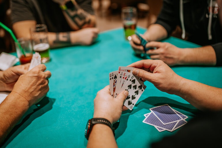 Players holding cards and drinking beer around a poker table, illustrating the connection between beer and game pace.