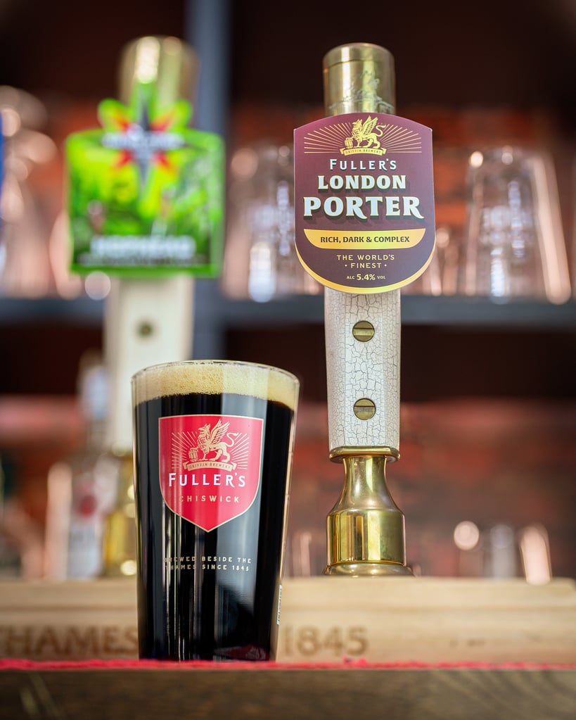 Fuller's London Porter in branded glassware next to tap handle in London pub.
