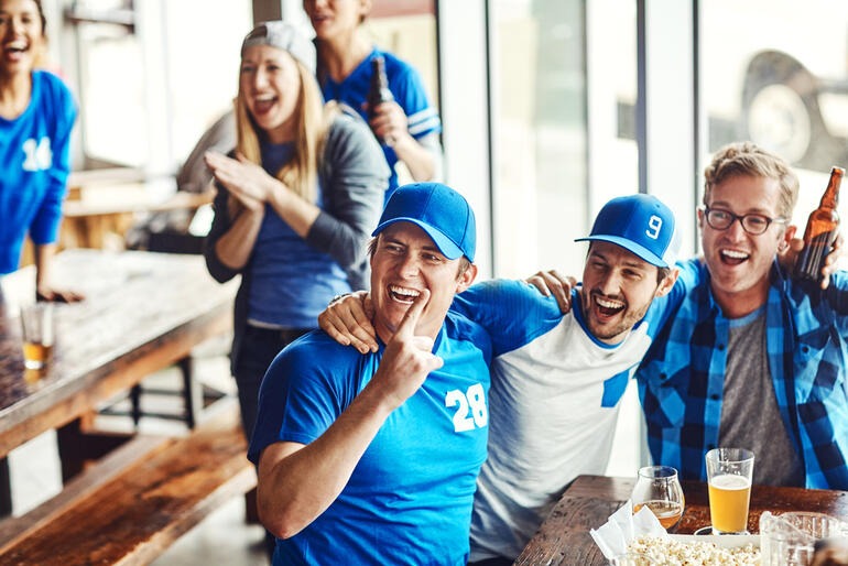 Friends enjoying beer together while watching a football game, cheering and laughing in a lively social setting.