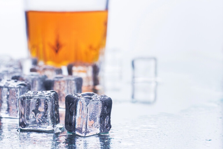Melting ice cubes beside a glass of beer on a wet bar surface.