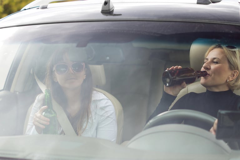 Two women drinking bottled beverages inside a vehicle during a brewery road trip.