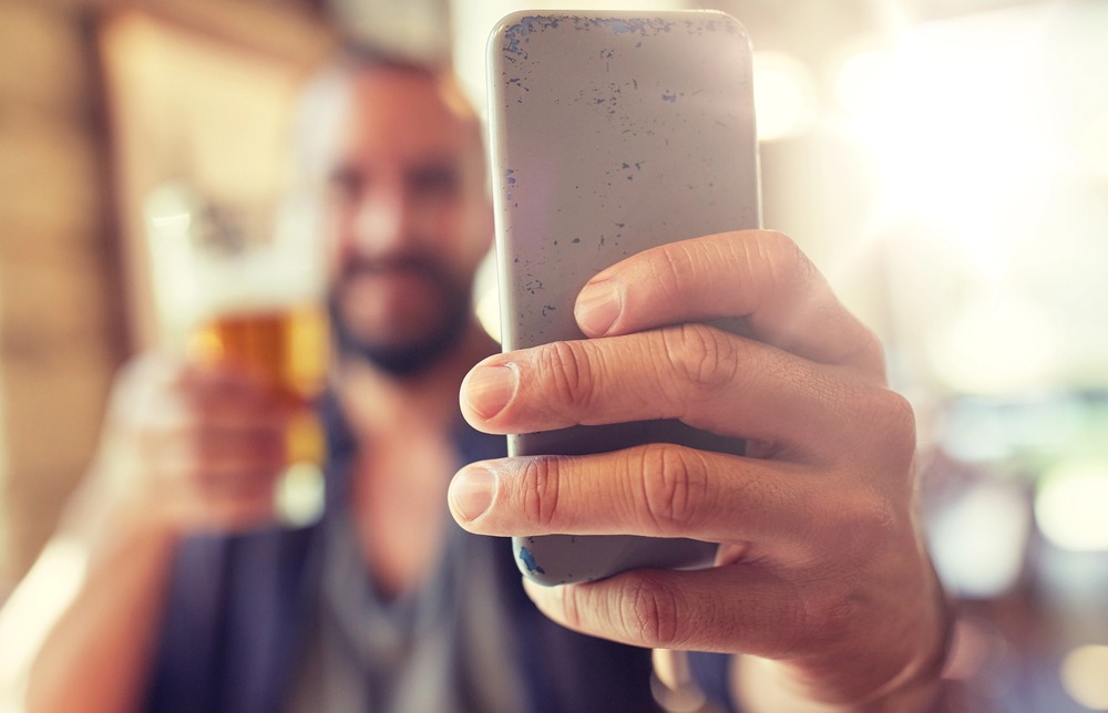 A beer enthusiast is shooting himself enjoying a glass of beer using his phone
