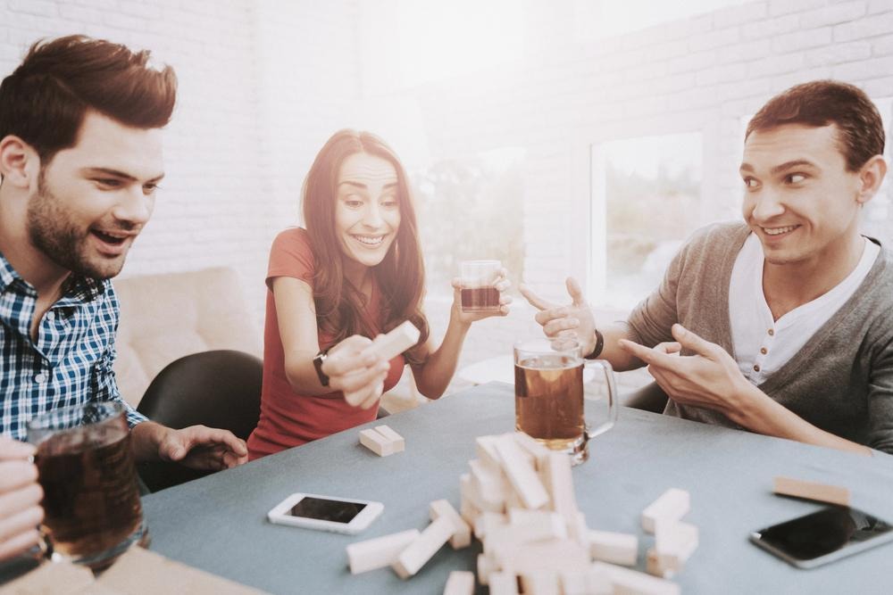 Friends have three people at a table, playing a game and laughing