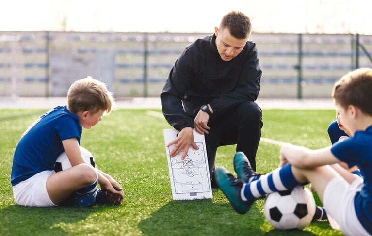 A male football coach showing a tactical diagram board to youth football players.