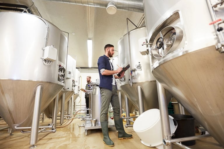 A man with a clipboard at a craft brewery or beer plant.