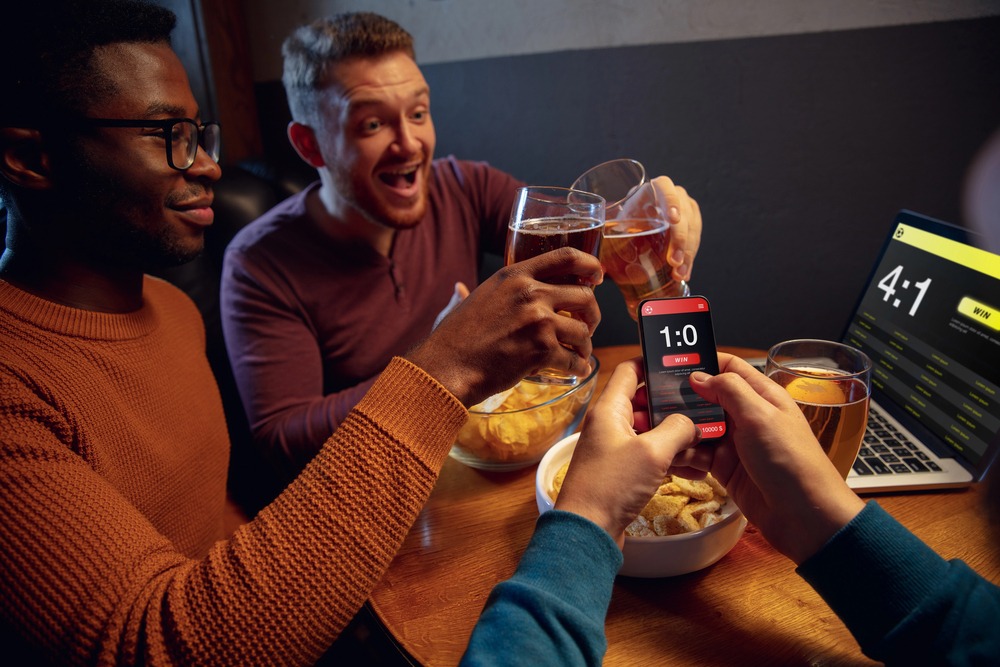 Friends enjoying beer with a web app for betting on their laptop.