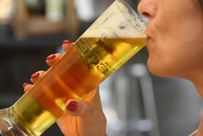 A close-up view of a man drinking a tall glass of cold golden beer with froth, to impress effect.