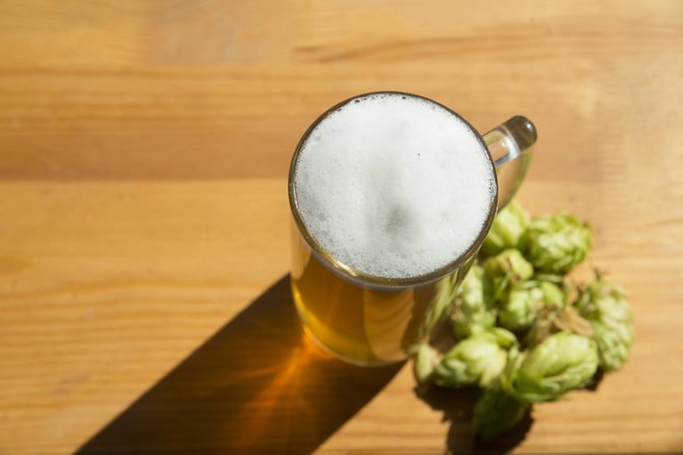 Dry-hopped beer in a glass beside hop pellets and fresh hop cones on a wooden table.