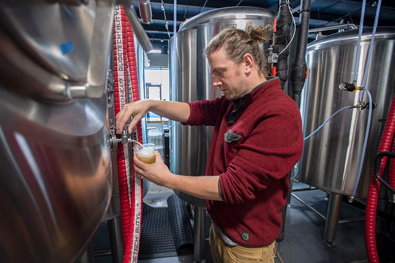 Brewer Peter Etges takes a sample out of a fermentor at Fayetteville Beer Works in Fayetteville, Arkansas