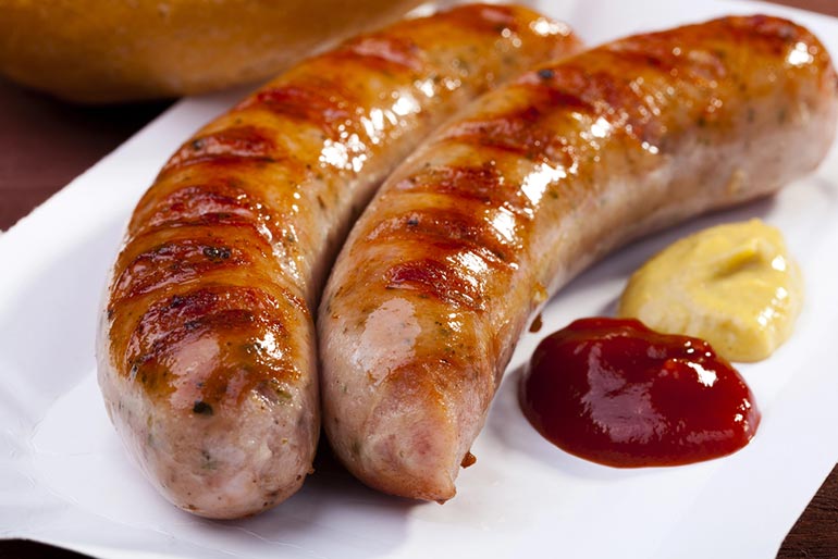 juicy brats on plate with ketchup and mustard beside