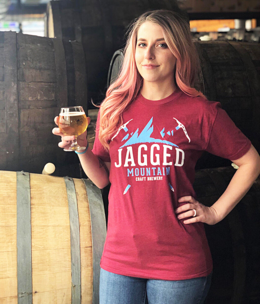 alyssa thorpe poses with a brew in front of barrels