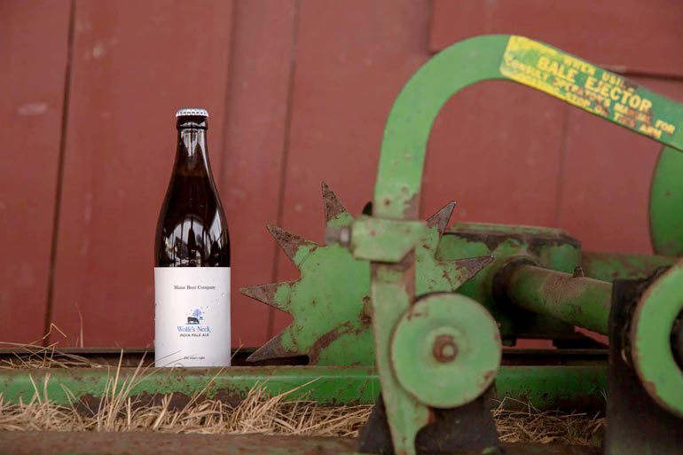 maine beer co wolfe's neck ipa next to barn and old farming equipment