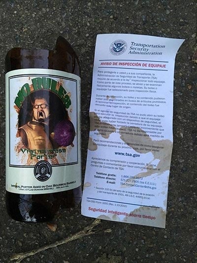broken bottle of Perrin Brewing No Rules next to TSA notice