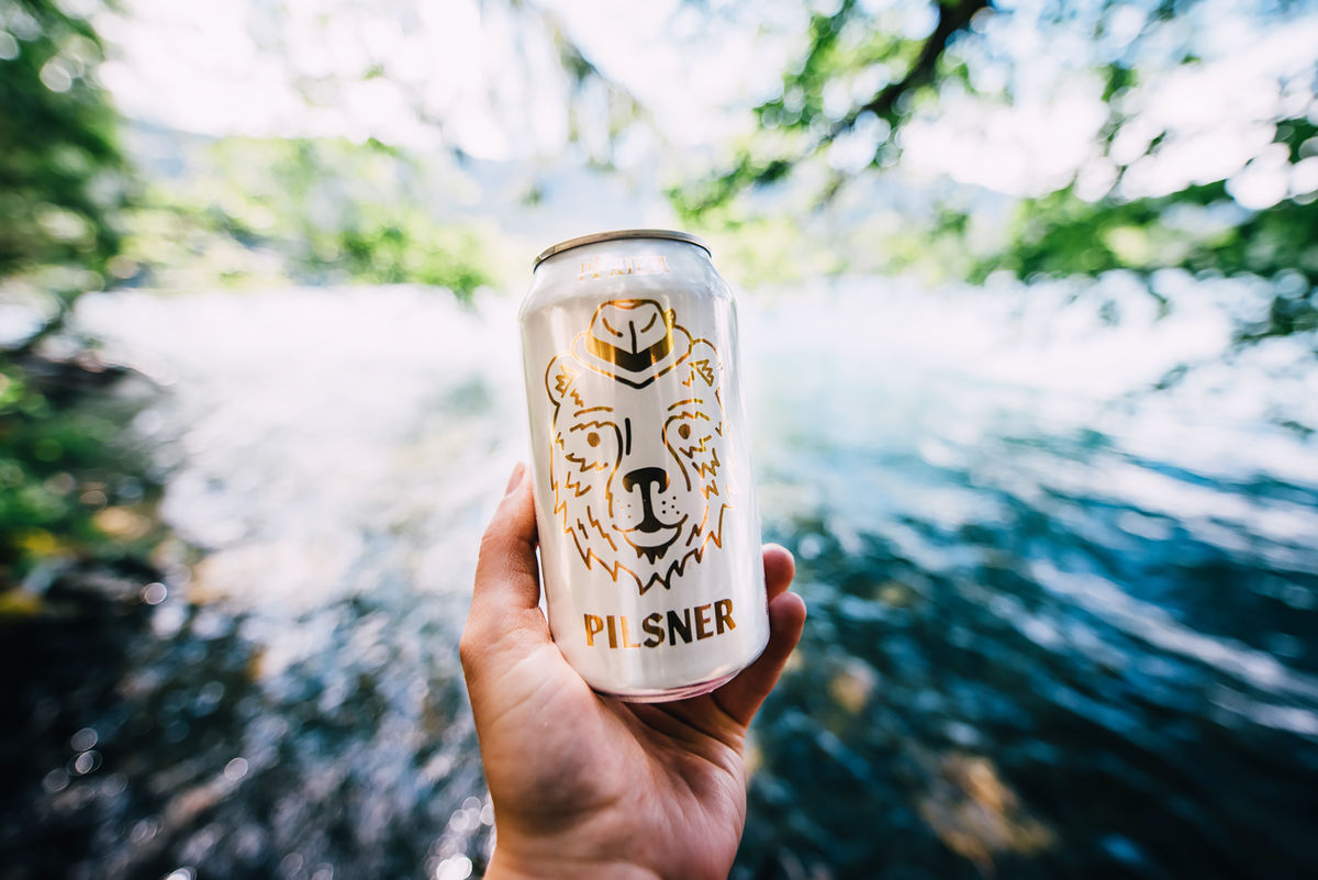 pfriem pilsner can held in front of a river
