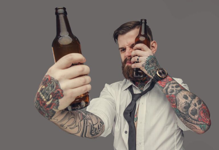 A man with tattoos holding two beer bottles