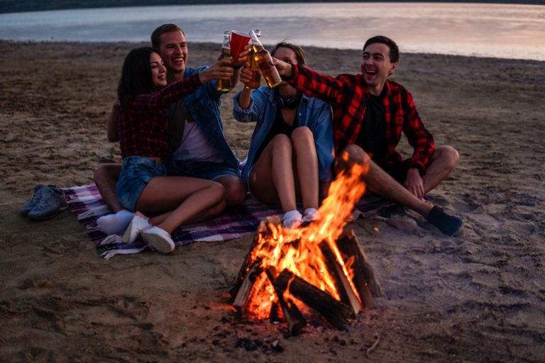 Friends joyfully toasting with beers while waiting for an amazing campfire night