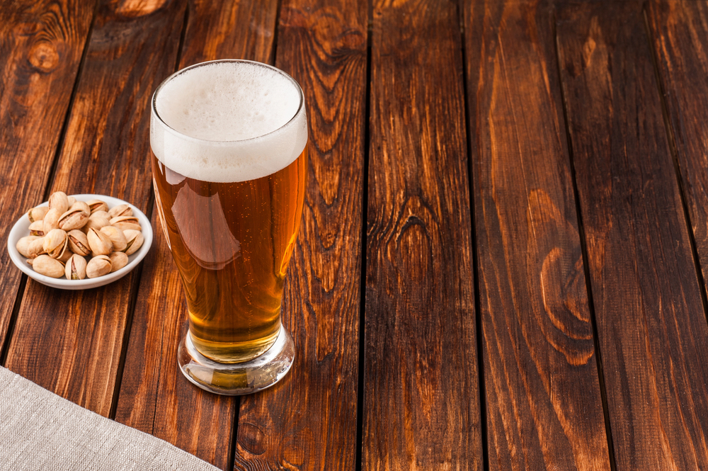 A Glass of light cold frothy beer and nuts on an old wooden table.