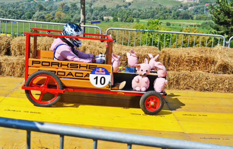 Racer driving a homemade soapbox car decorated with toy pigs at the Red Bull Soapbox Race.